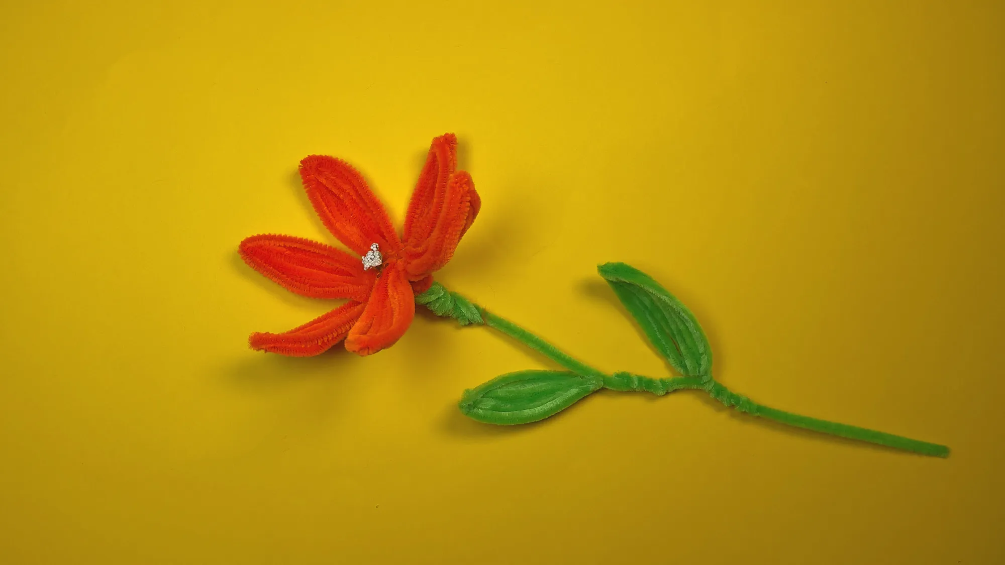 DIY Lilienblume aus Chenilledraht Schritt 3: Grüne Blätter am Stiel befestigen, Blüte anbringen und nach Wunsch verzieren – fertige Pfeifenputzer-Blume