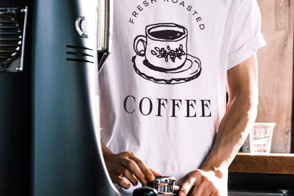 Máquina de café, hombre con una camiseta en la que está impreso el logotipo de una cafetería