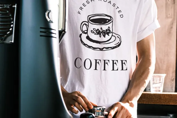 Kaffeemaschine, Mann mit einem T-Shirt, auf dem ein Logo einer Kaffeebar aufgedruckt ist