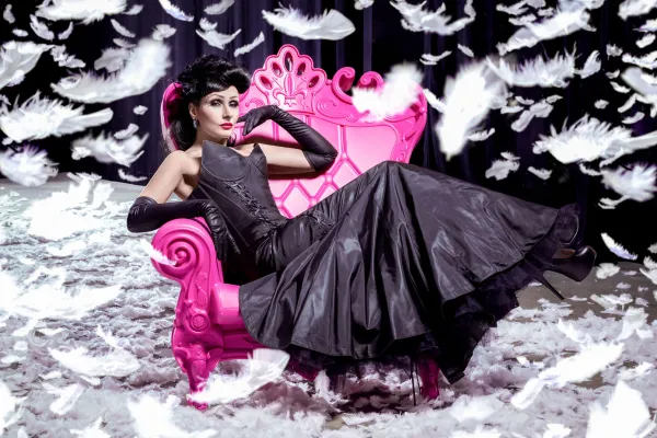 Beispiel zur Beauty-Retusche in Photoshop: Frau auf einem rosa Stuhl, umgeben von fallenden Federn