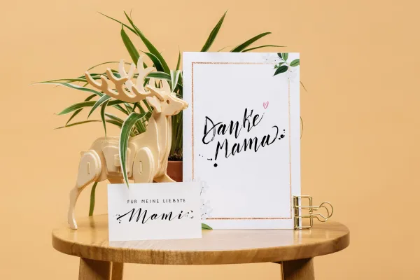 Muttertagskarten mit Handletterings in verschiedenen Größen auf einem Tisch vor Blumen